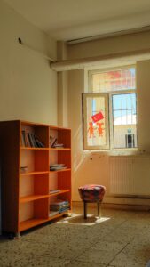 Sunlit classroom with open window displaying Turkish flag art, books neatly organized in shelf.