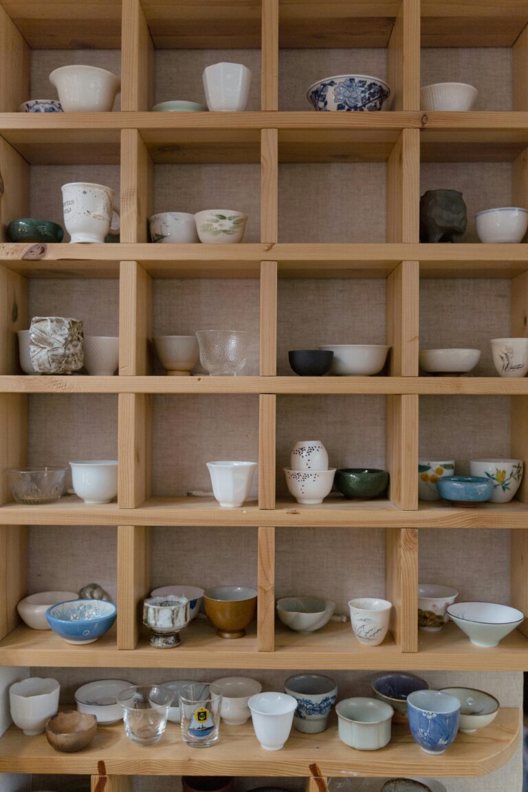 An array of ceramic cups displayed on a wooden shelf, ideal for art decor.